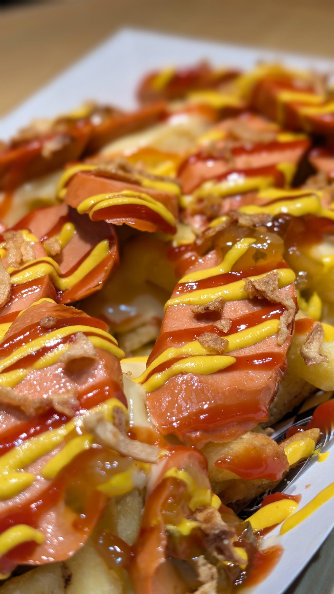 Close-up of hot dog loaded fries with ketchup, mustard, cheese sauce and crispy onions